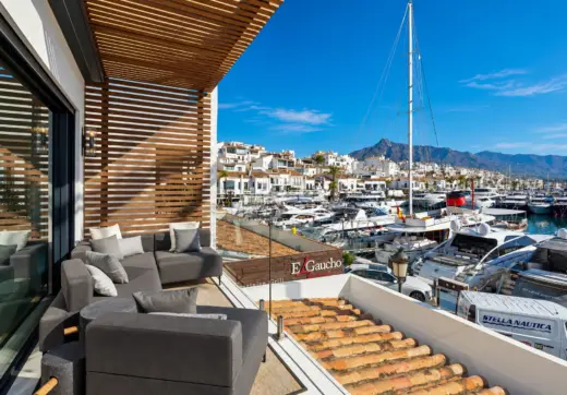 Apartament na sprzedaż w Puerto Banús – elegancki taras z szarymi sofami, drewnianą pergolą i panoramicznym widokiem na luksusowe jachty oraz góry.