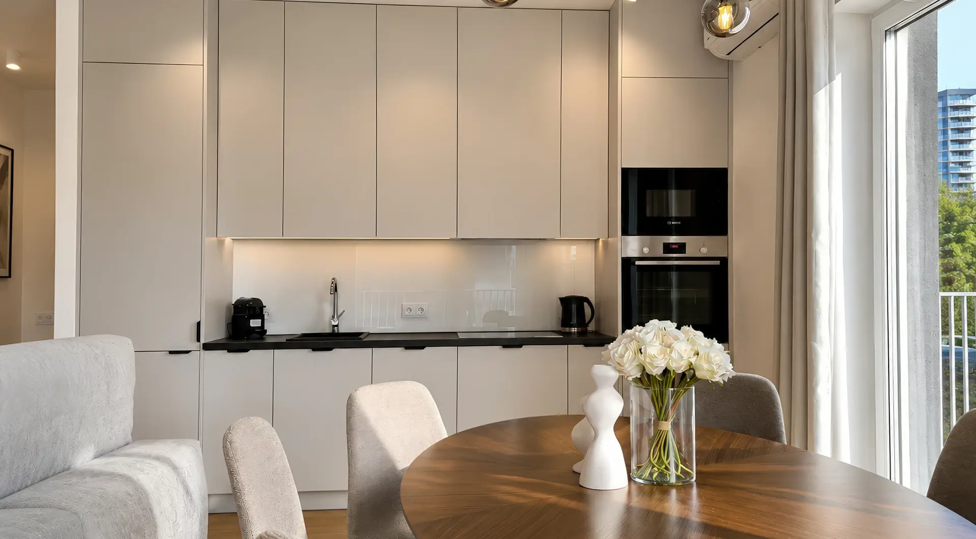 Elegancki apartament Warszawa Wola – jasna kuchnia z zabudową na wymiar, drewnianym stołem jadalnianym oraz dużymi przeszkleniami zapewniającymi naturalne światło.