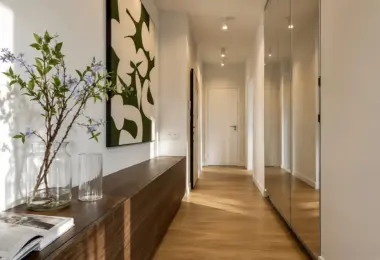 Elegancki apartament Warszawa Wola – nowoczesny hol wejściowy z pojemną zabudową szaf, drewnianą podłogą oraz designerskimi dekoracjami ściennymi.