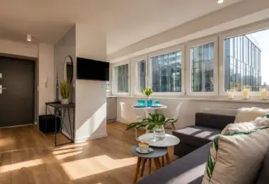 Apartament Warszawa Śródmieście z nowoczesnym salonem, częścią jadalnianą, dużymi oknami oraz widokiem na nowoczesną zabudowę centrum miasta.