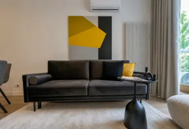 Mieszkanie Domaniewska wynajem, nowoczesny salon z czarną sofą, designerskim obrazem i stolikiem kawowym