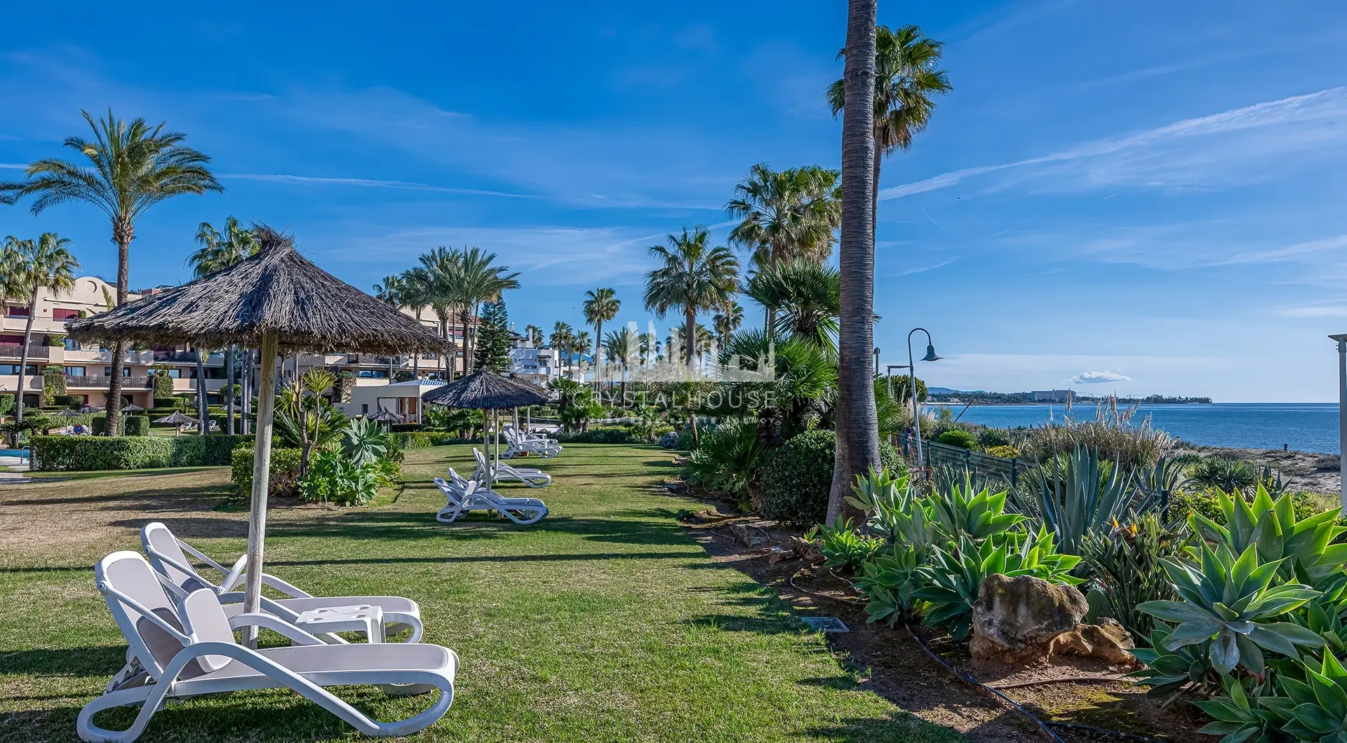 Luxury beachfront apartment in Estepona beachfront garden with sun loungers and palm trees by the Mediterranean Sea