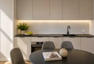 Apartament Holm Skanska – minimalistyczna kuchnia w zabudowie z jadalnią, okrągłym stołem oraz wysokiej jakości wyposażeniem w nowoczesnym stylu.