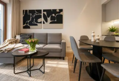 Apartament Holm Skanska – jasny salon połączony z jadalnią, wyposażony w elegancką sofę, designerskie stoliki kawowe oraz nowoczesny stół z krzesłami.