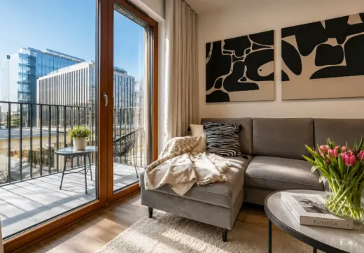 Apartament Holm Skanska – elegancki salon z wyjściem na przestronny taras, dużymi przeszkleniami oraz widokiem na nowoczesną zabudowę biurową Mokotowa.