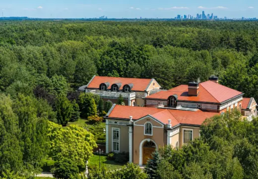 Luksusowa rezydencja pod Warszawą z widokiem z lotu ptaka, prywatnym pałacem otoczonym lasem, czerwonym dachem i panoramą Warszawy w tle
